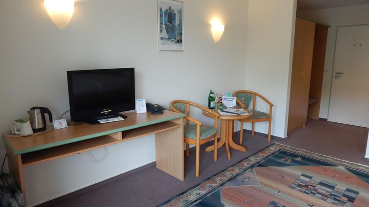 Ein einfaches Hotelzimmer mit einem Fernseher, einem Tisch und zwei Stühlen. Der Raum ist hell und freundlich gestaltet.