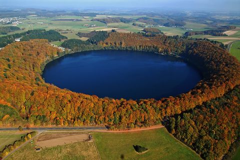 Luftaufnahme des Pulvermaars, umgeben von herbstlich gefärbtem Wald.