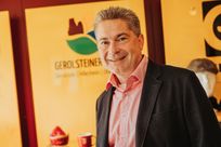 Ein schick gekleideter Herr mit Hemd und Sakko lächelt in die Kamera. Hinter ihm das Logo der Touristik GmbH Gerolsteiner Land und einige Souvenierartikel.