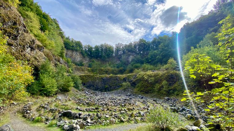 Interior of the Arensberg volcano with rocks and vegetation under a cloudy sky.