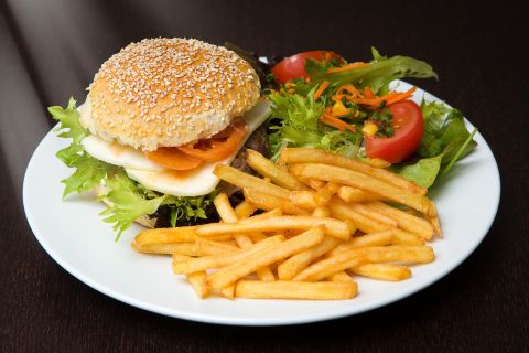 <p>Ein saftiger Burger mit Käse, Tomaten udn Salat belegt, auf einem weißen Teller. Daneben Pommes Frittes und einige Salatblätter und Tomaten.</p>