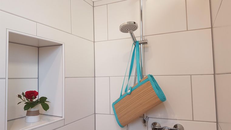 Eine moderne Duschkabine mit weißen Fliesen und einer Dusche in der Mitte. In einer Nische steht eine kleine Blume in einem Topf.