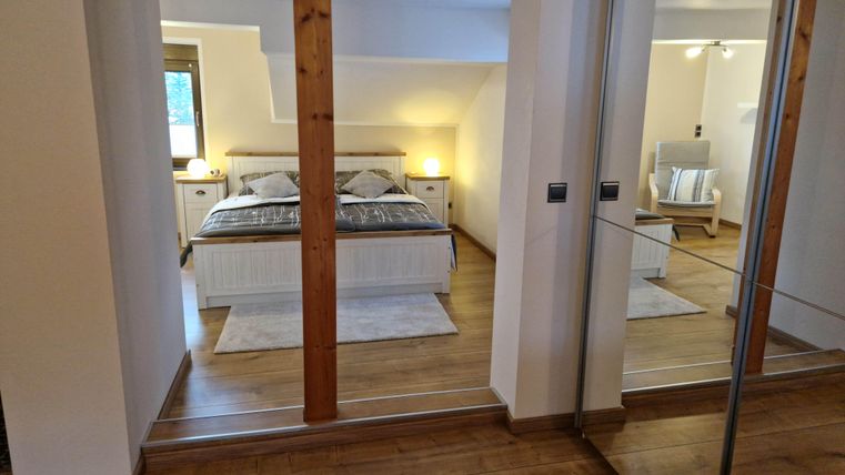 Ein gemütliches Schlafzimmer mit einem großen Bett und modernen Möbeln. Es gibt auch einen bequemen Sessel und angenehmes Licht.