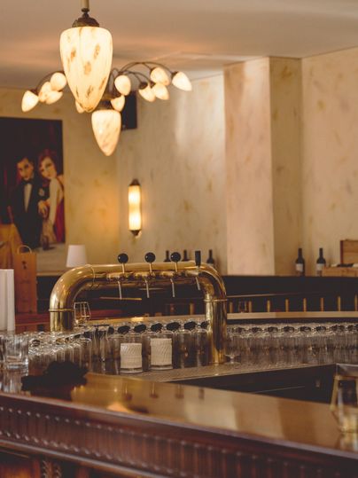 A stylish bar with a shiny tap and a row of glasses. Beautiful lamps and a painting can be seen on the walls.