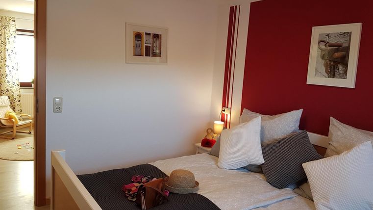 Ein gemütliches Schlafzimmer mit einem großen Bett und bunten Kissen. Die Wände sind teilweise rot gestrichen und die Dekoration wirkt einladend.