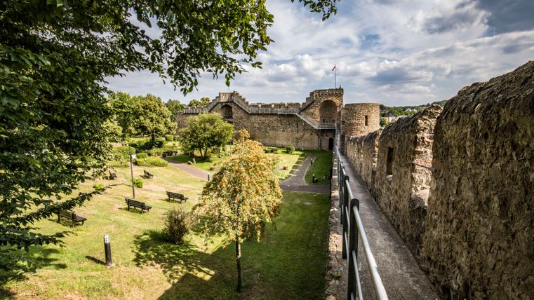 Blick auf eine historische Stadtmauer mit Garten und Bäumen im Vordergrund.