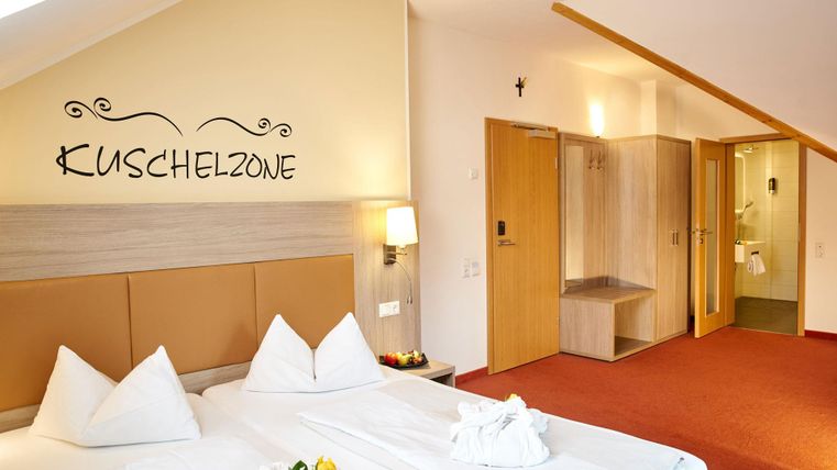 A cozy bedroom with a large bed and white pillows. The walls are light-colored, and there is an adjoining area with a shower and toilet.