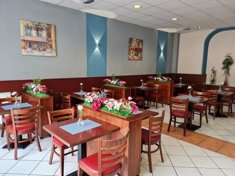 Gemütlicher Restaurantinnenraum mit Holztischen, roten Stühlen und Blumenarrangements. An den Wänden hängen Bilder, der Boden ist gefliest.