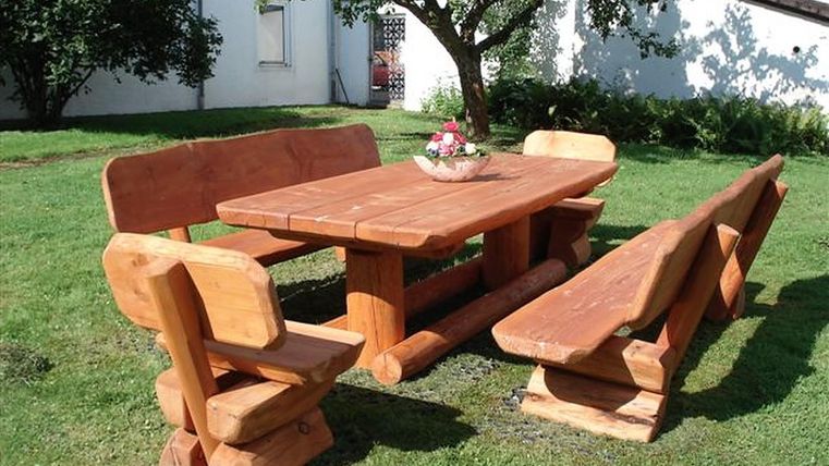 Une table en bois rustique avec des bancs se trouve dans un jardin verdoyant. Au centre de la table se trouve un petit bouquet de fleurs.