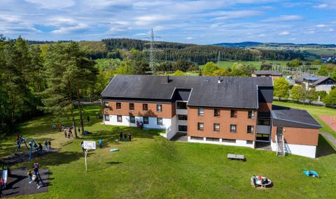 Ein Ausblick von oben auf das Gebäude der Jugenherberge Gerolstein. Drum herum ist eine grüne Wiese, Kinder spielen darauf!