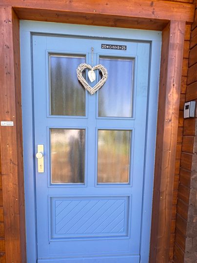 Eine blaue Haustür mit vier Fenstern und einem herzförmigen Deko-Element. Die Tür befindet sich in einem Holzrahmen.