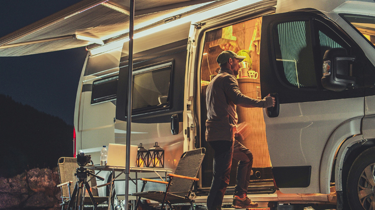 Eine person steigt in sein Wohnmobil ein. Draußen ist es dunkel, das Licht im Innenraum ist an. Es ist ein Pavillon an der Seite des Wohnmobils gespannt.