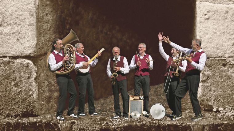 Gruppenbild der Musiker. Einzelne spielen auf ihren Instrumenten andere jubeln.
