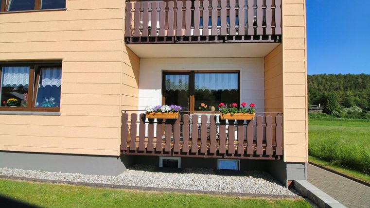 Ein Balkon an einem mehrstöckigen Haus mit Blumenkästen. Die Fassade ist in einem warmen Farbton gehalten.