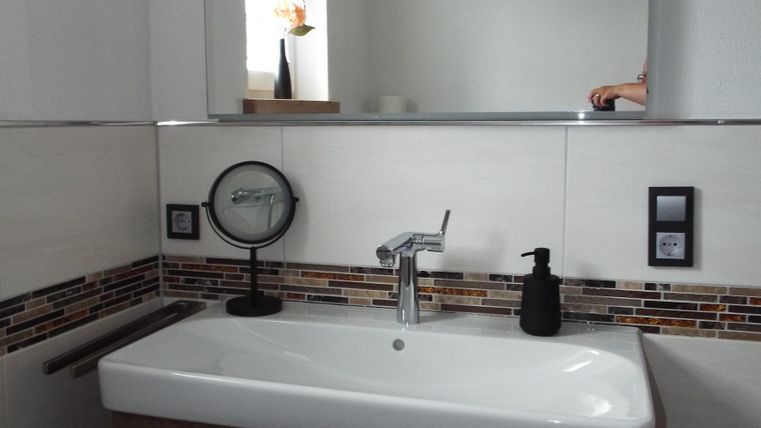 Ein modernes Badezimmer mit einem eleganten Waschbecken und einem Holzunterbau. Im Hintergrund ist ein Spiegel und ein Fenster sichtbar.