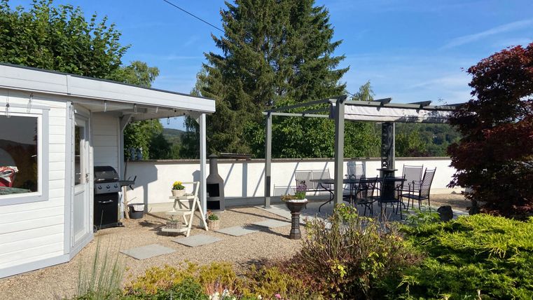 Ein gemütlicher Gartenbereich mit einer Terrasse und einem Grill. Umgeben von bunten Blumen und Bäumen, bietet der Ort eine entspannte Atmosphäre.