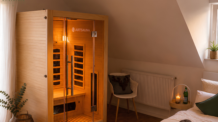 A modern infrared sauna in a stylishly furnished room. The room is cozy, designed with a chair, plants, and soft lighting.