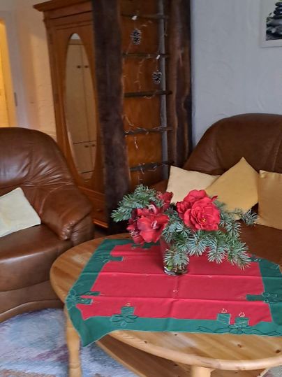 Ein gemütliches Wohnzimmer mit zwei braunen Ledersesseln und einem runden Tisch. Auf dem Tisch liegt eine festliche Tischdecke mit roten und grünen Akzenten sowie Weihnachtsdekoration.