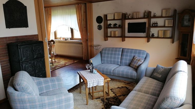 A cozy living room with blue sofas and a small table. On the wall are shelves with books and accessories.