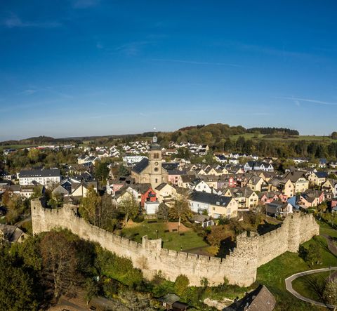 Une ville historique avec des remparts bien conservés et une église au centre. Entourée de collines verdoyantes et de maisons modernes.