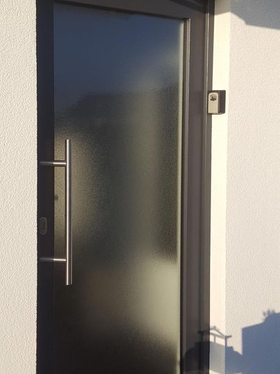 Eine moderne Eingangstür aus mattem Glas mit einem schlanken Edelstahlgriff. Die Tür ist in eine helle Wand integriert und wirkt einladend.