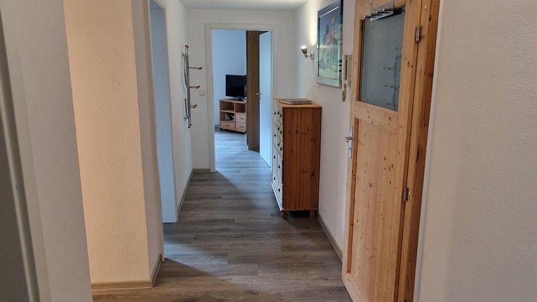 Un hall lumineux avec un sol en bois et deux portes sur les côtés. Au bout du hall, une autre pièce est visible.