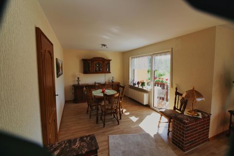 Ein gemütlicher Wohnraum mit einem Esstisch und Stühlen. Große Fenster lassen viel Licht herein und bieten Zugang zu einem Balkon.