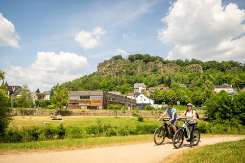 Ein Mann und eine Frau fahren auf Fahrrädern bei schönem Wetter durch den Kurpark Gerolstein mit Dolomitfelsen im Hintergrund.