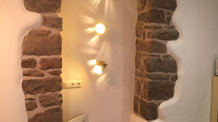 Une pièce confortable avec une arche en pierre structurée et un éclairage doux. Le sol est clair et moderne, ce qui crée une atmosphère accueillante.