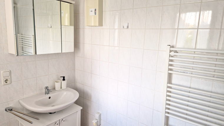 Une salle de bain moderne avec des carreaux blancs et un lavabo. Dans la pièce se trouve un miroir et un porte-serviettes.
