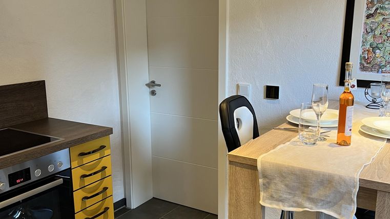 Een moderne keuken met gele kasten en een houten bar. Op de bar staan gedekte borden en een fles drank.