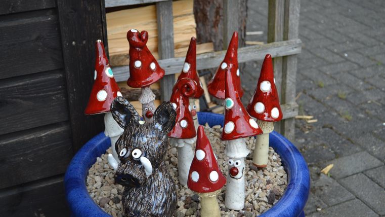 Keramikkunst mit roten Pilzen und einem Wildschwein in einem blauen Topf.