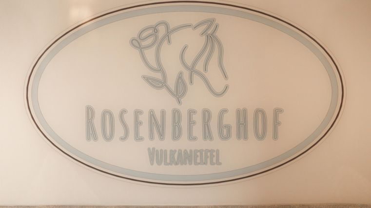 Ein Schild mit dem Schriftzug "ROSENBERGHOF" und der Zusatz "VulkanEifel". Das Design zeigt eine stilisierte Darstellung eines Tieres.