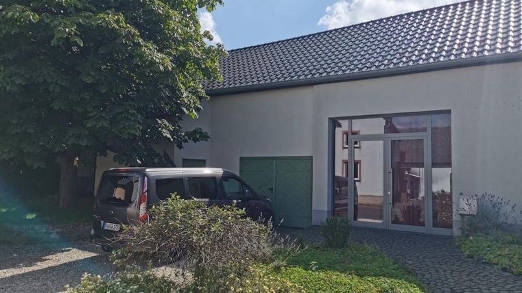 Een modern huis met een bestrate oprit en een groene tuin. Een zwarte auto staat voor het gebouw onder een grote boom.