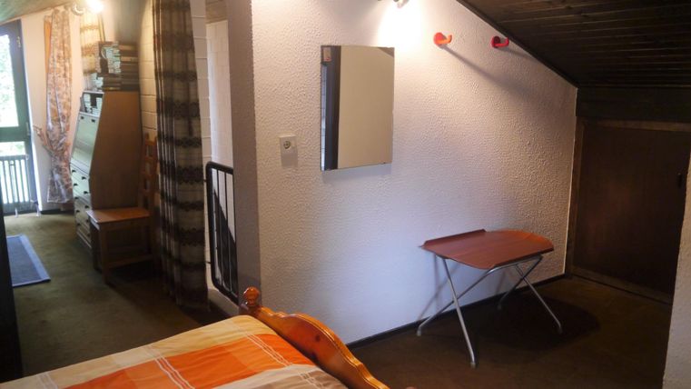 Ein helles Zimmer mit einem Doppelbett und einem kleinen Tisch. Es gibt einen Spiegel an der Wand und einen Blick auf den Balkon.