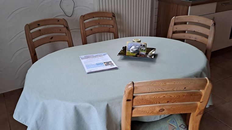 Ein runder Tisch mit einer hellen Tischdecke steht in einem Raum. Darum sind vier Holzstühle angeordnet.