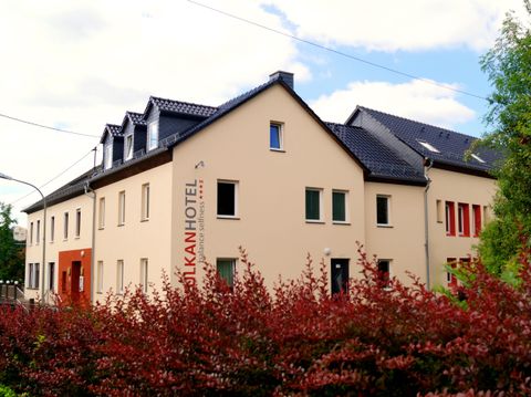 Un bâtiment hôtelier moderne avec un design clair et accueillant. Au premier plan, on peut voir des buissons colorés qui créent une atmosphère invitante.