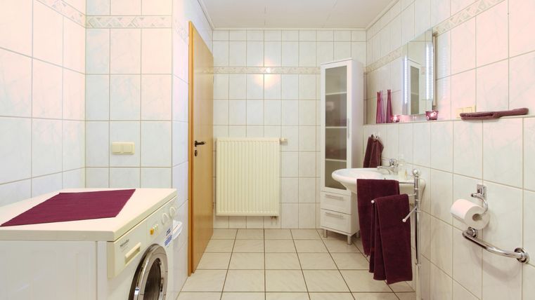 Ein modernes Badezimmer mit weißer Fliese und einem Fenster. Eine Waschmaschine, ein Waschbecken und Handtücher in lila sorgen für eine gemütliche Atmosphäre.