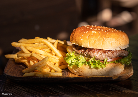 A juicy burger with a sesame bun, lettuce, and tomato is placed on a wooden board. Next to it are crispy French fries.