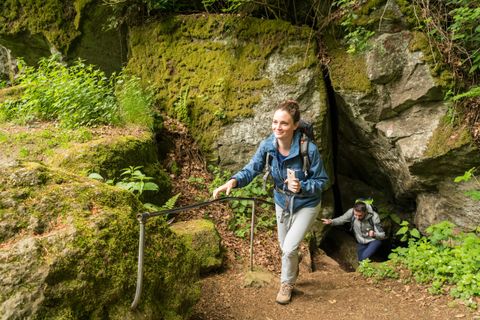Deux randonneurs sortent d'une grotte recouverte de mousse. Une femme à l'avant sourit en montant un escalier. Un homme la suit.