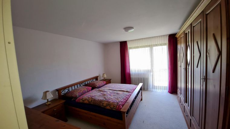 A cozy bedroom with a double bed and a large wardrobe. Large windows let in plenty of light and create a bright atmosphere.