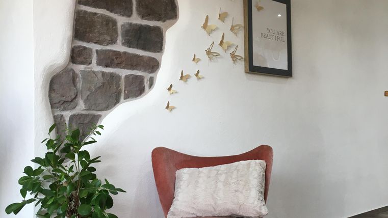 Une pièce confortable avec un fauteuil rouge, une plante et un mur décoratif en pierres. Des petits avions en papier sont fixés au mur.