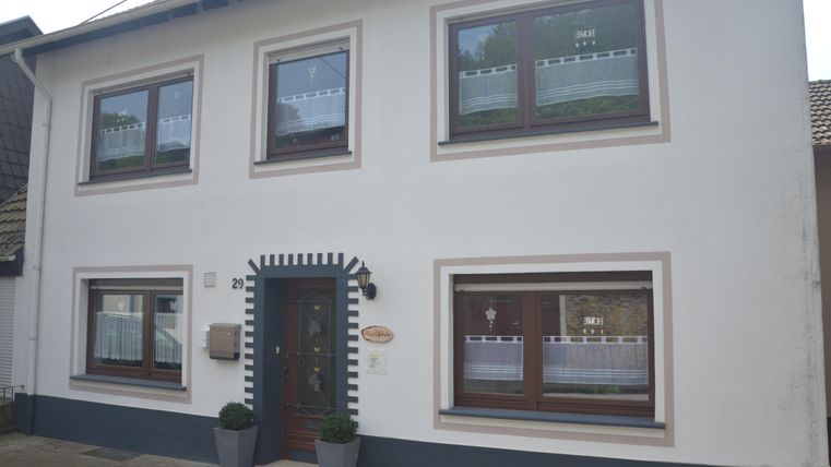 Een modern, tweeledig woonhuis met witte muren en bruine ramen. Voor de deur staan twee plantenbakken met groene planten.