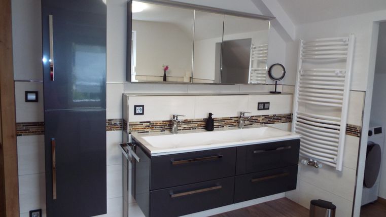 Ein modernes Badezimmer mit einem stilvollen Waschbecken und großem Spiegel. Die Einrichtung ist in dunklen Farbtönen gehalten und hat elegante Details.