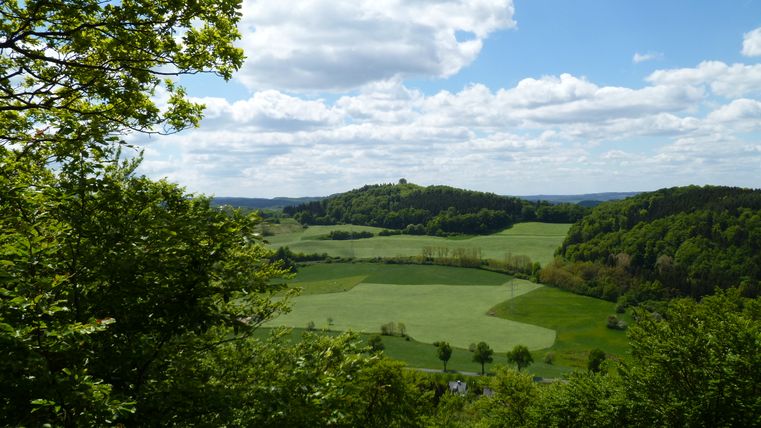 Landschaft mit grünen Feldern und Hügeln unter blauem Himmel mit Wolken.