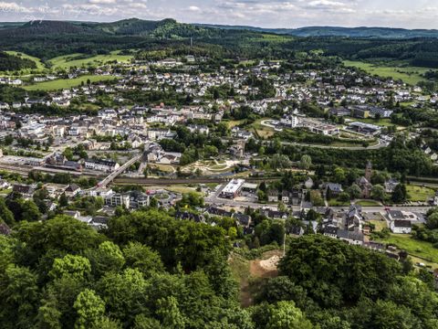 Eine malerische Stadtlandschaft mit grünen Hügeln im Hintergrund. Die Straßen und Gebäude sind gut sichtbar und verleihen der Szene eine ruhige Atmosphäre.