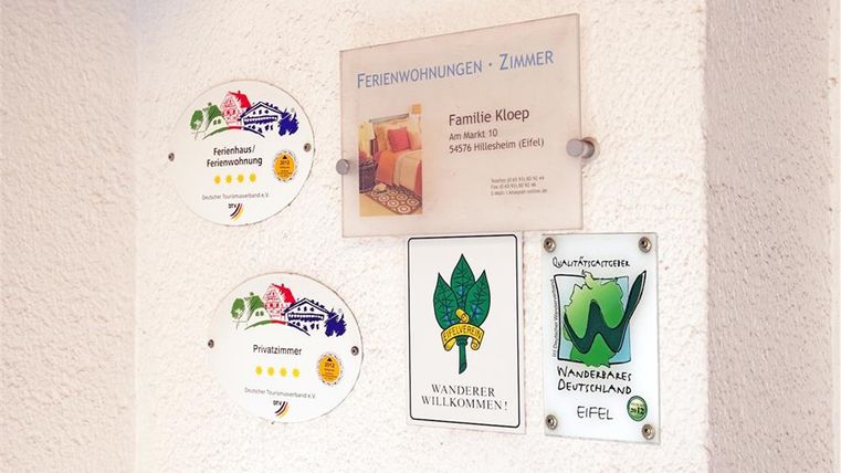 Ein Schild mit Informationen zu Ferienwohnungen und Auszeichnungen. Es zeigt die Kontaktdaten der Familie Kloep sowie verschiedene Qualitätszeichen für die Unterkunft.