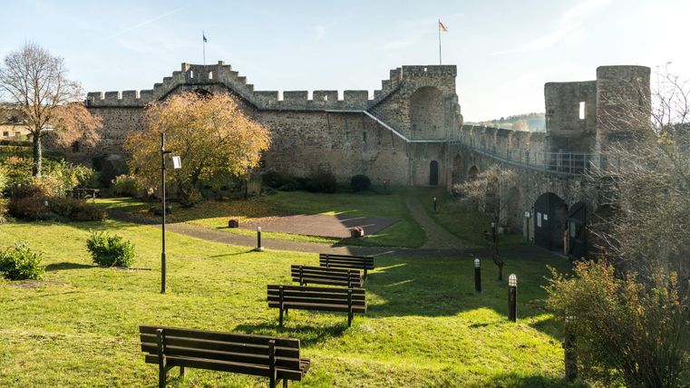 Historische Stadtmauer in Hillesheim mit begehbarem Weg, umgeben von einem grünen Park mit Bänken und Bäumen.
