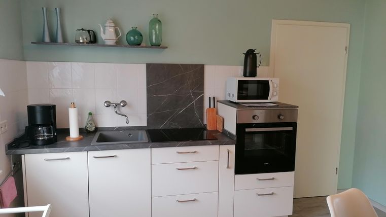 Eine moderne Küche mit weißen Schränken und einer grauen Arbeitsplatte. Sie verfügt über einen Herd, eine Mikrowelle und Kochutensilien.