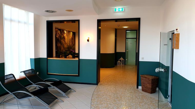 A peaceful wellness area with lounge chairs and light-colored walls. The reception is clearly visible, and there is access to other rooms.